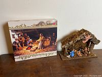 Rustic crèche manger with bark roof and figurines inside, arranged as nativity scene.