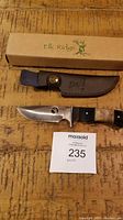 Elk Ridge cutting knife with leather sheath and branded box on wooden surface