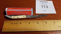 Open knife with blade extended, placed beside a wooden ruler indicating about 5 inches length, next to its box and lot number card.