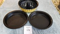 Three bakeware items displayed on a towel: one yellow and black Bundt pan and two black round cake pans.