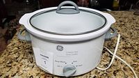 General Electric white 3 quart oval slow cooker crock pot with transparent glass lid and gray handle on countertop.