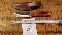 Knife with wooden handle and leather sheath laid flat with a ruler showing approximately 8 inches in length.