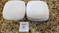 Six stacked, square white glass dinner plates on a kitchen counter.