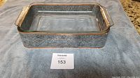 Elegant rectangular glass baking pan inside a hammered metal holder with copper trim, placed on a towel surface.