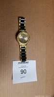 Full length view of the Geneva men's wrist watch displaying the black and gold tone band and round gold dial.
