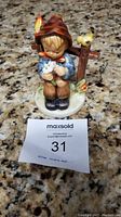 Front view of Hummel figurine showing boy holding a flower, sitting next to a post with a bird.