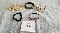 Five assorted bracelets on grey fabric showing varied styles and materials