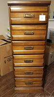 Front view of a vintage wooden dresser with six drawers and brass handles.
