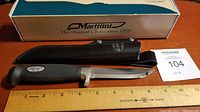 Full view of Marttiini 8" fillet knife with black handle alongside its sheath and box, placed next to ruler for size reference.