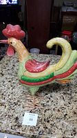 Side view of colorful painted metal rooster sculpture showing detailed head, comb, wattle, and body colors.