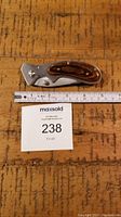 Photo of folded pocket folding knife with wooden handle next to measurement ruler showing size about 4 inches folded.