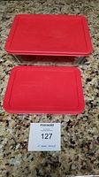 Two Pyrex glass pans topped with solid red lids, smaller on left front, larger on back right.