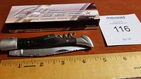 Photo showing the closed pocket knife with dark handle and metal ends, lying next to a ruler showing approximately 8.5 inches length.