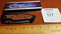 Opened box and closed knife sitting on a ruler showing length approx. 8 inches with packaging labeled Rite Edge World's Premier Knife Company.