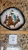 Ceramic decorative plate, free form shape with mid-century modern pagoda scene, ruler placed for size reference.