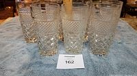 Seven clear cut glass tumblers arranged on a blue towel, showing the detailed textured diamond and etched pattern of the glassware.
