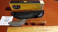 Photo of Buck knife with wooden handle, nylon sheath, ruler for size reference, and original yellow box.