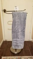Front view of a freestanding towel holder holding one blue towel, positioned against a door.