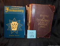 Two books side by side: The older 'History of Freemasonry and Concordant Orders' book with a worn brown cover and the newer 'A Dictionary of Freemasonry' book with a blue dust jacket.