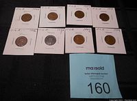 Nine USA pennies dated 1919 to 1949 in white protective cardboard holders with labels, arranged on black surface.