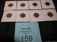 Eight USA pennies from 1946 to 1955 in individual white cardboard coin holders labeled with year and mint mark on black background.