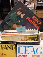 Photo of vinyl record box with various album covers showing Rolf Harris large album in back, and multiple records stacked inside box with visible edge wear.