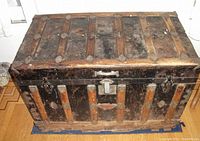 Front and side view of antique metal and wood trunk showing vertical wood slats and metal hardware, including lock and carrying handles.