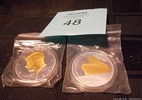 Four commemorative coins in plastic cases, two JFK and two Titanic themed coins with gold accents.