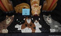 Photo showing full set of five flat painted wood cat ornaments arranged in front in a row, with two tall carved wooden cat statues behind them.