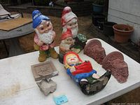 Overview of lot showing three garden gnomes, flower girl gnome, two goddess shelves, sun plaque, and seagull on rock.