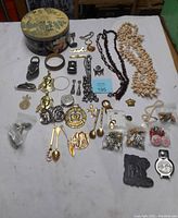 Wide shot showing the full assortment of jewelry, pins, necklaces, small bags of jewelry parts, a watch, a small lion figurine, and the vintage Peckfrean tin used to store the items.