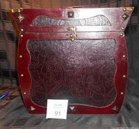Front view showing curved front panel, stud decoration, latch closure, and overall reddish tone