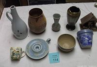 Overview of nine assorted stoneware and china items including vases, cups, a bowl, a candle holder, and a small house figurine on a table.