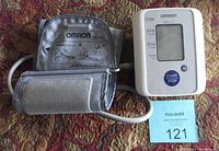 Photo of the Omron blood pressure monitor and attached arm cuff, showing the device's digital screen and control buttons.