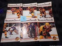 Six Vancouver Canucks hockey magazines from the 1980s shown laid out in two rows of three on a black surface. Each magazine features hockey action or posed player images on the cover with the title 'Vancouver Canucks Hockey Magazine' at the top.
