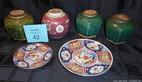 Six pieces of Asian china or pottery displayed including three green hexagonal jars on the top and front two colorful ceramic plates.