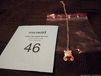 Sterling silver chain with attached small bear-shaped charm in silver and gold, placed on a dark surface with auction lot tag visible.