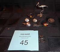 Photo showing the lot items arranged on a dark cloth, including cufflink, metallic buttons, pins, and silver-tone bird figurine