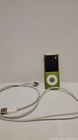 Green Apple iPod Nano 4th Generation alongside white USB charging cable against plain background.