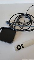 Apple TV Module with power cable and Apple remote control placed on a white surface.