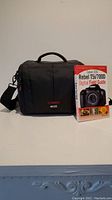 Front view of black Canon EOS camera bag with attached shoulder strap and Canon Rebel T5i/700D Digital Field Guide book standing beside it.
