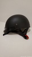 Side angle view of matte black CKX Slick half shell motorcycle helmet showing smooth surface and chin strap.