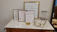 Photo showing four gold frames of varying sizes along with gold card stands and a gold metal frame tray on a marble surface for event decoration.