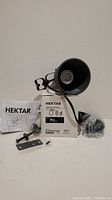 Black metal Ikea HEKTAR wall mount lamp, conical shade, power cord, screws, and instruction manual on white surface.