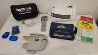 Photo showing MEC cotton sleepbag liner packed in its bag, Hotcore camp pillow in black bag, Italy maps, Corona quickdry towel, battery operated lightbulb keychain, Lewis n Clark body belt, and three packs of Coleman sheets along with three compressed camp towels.