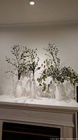 Three white vases with etched line detail on mantel with dried eucalyptus branches