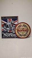 Two metal decorative signs - rectangular motorcycle image with Union Jack and circular Norton logo sign.