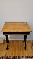 Front view of old fashioned desk showing wooden top with circular holes and metal legs with claw feet.