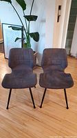 Front view of two dark grey fabric chairs with black legs, showing quilted seat and back design.