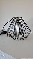 Full view of black wireframe geometric pendant light with long black cord and wall plug.